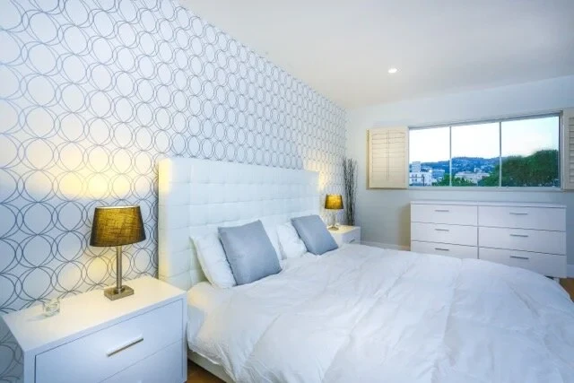 Master bedroom with white tufted headboard, geometric wallpaper and city views