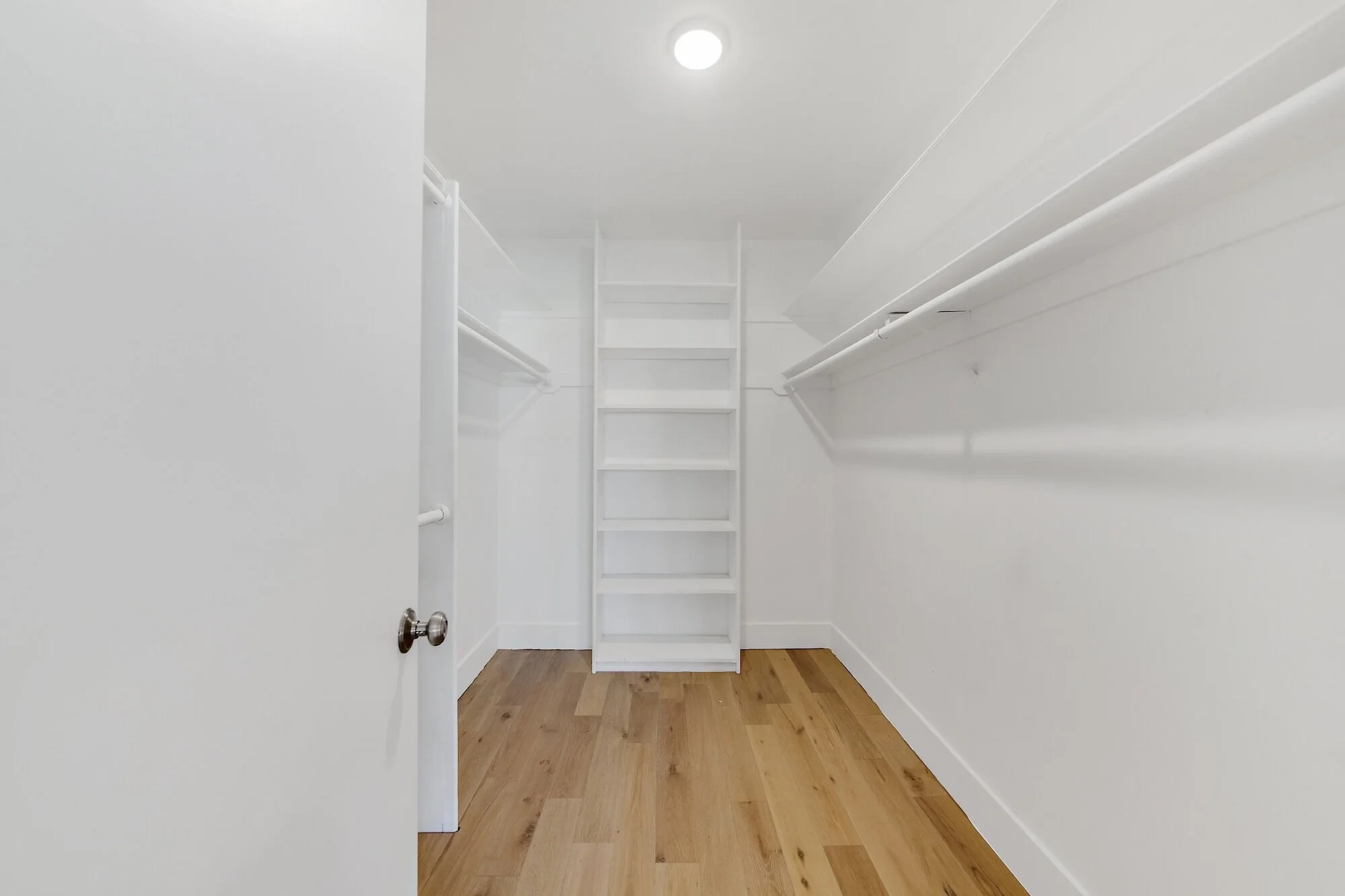 Walk-in closet with white built-in shelving and hardwood floors