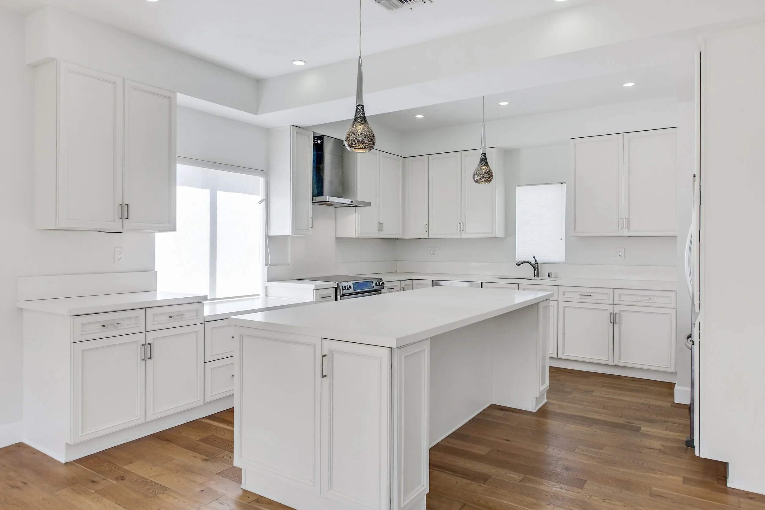 Bright white kitchen with large island, pendant lights and hardwood floors