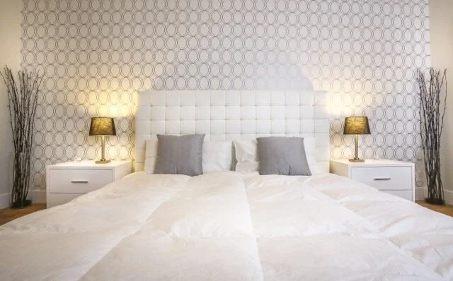 Master bedroom with white upholstered headboard and geometric wallpaper