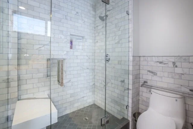 Spa shower with marble subway tile, glass enclosure and bench seat